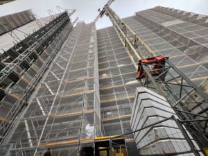 Baustelle mit Gerüst und Kran, Fortschritt Hochhausbau, moderner städtischer Wohnraum im Bau.