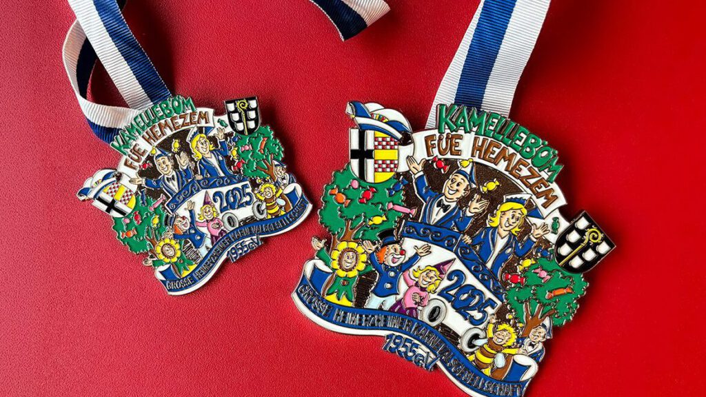 Kamelleböm-FB-Webseite_3_reduziert Karnevalsorden 2025 mit buntem Design, blau-weißer Band auf rotem Hintergrund. Thema: Kamellebom füe Hemezem.