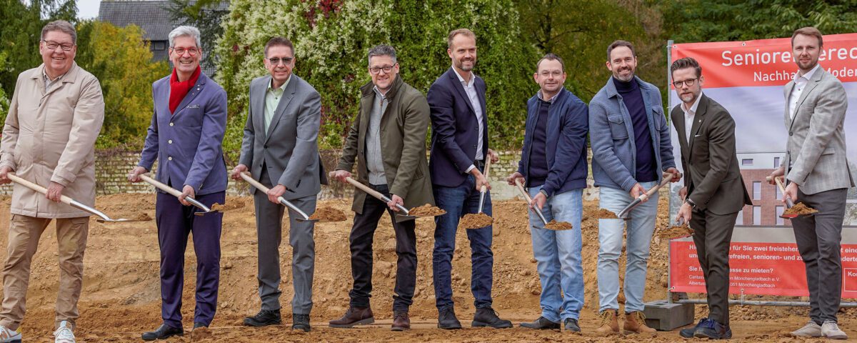 Gruppe bei Spatenstich für Seniorenresidenz, grüner Hintergrund, nachhaltiges Bauen, Herbst.