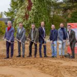 Gruppe bei Spatenstich für Seniorenresidenz, grüner Hintergrund, nachhaltiges Bauen, Herbst.