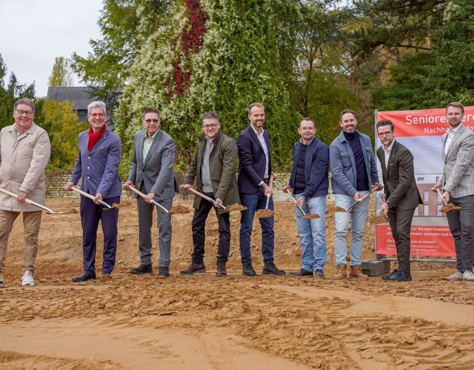 Gruppe bei Spatenstich für Seniorenresidenz, grüner Hintergrund, nachhaltiges Bauen, Herbst.
