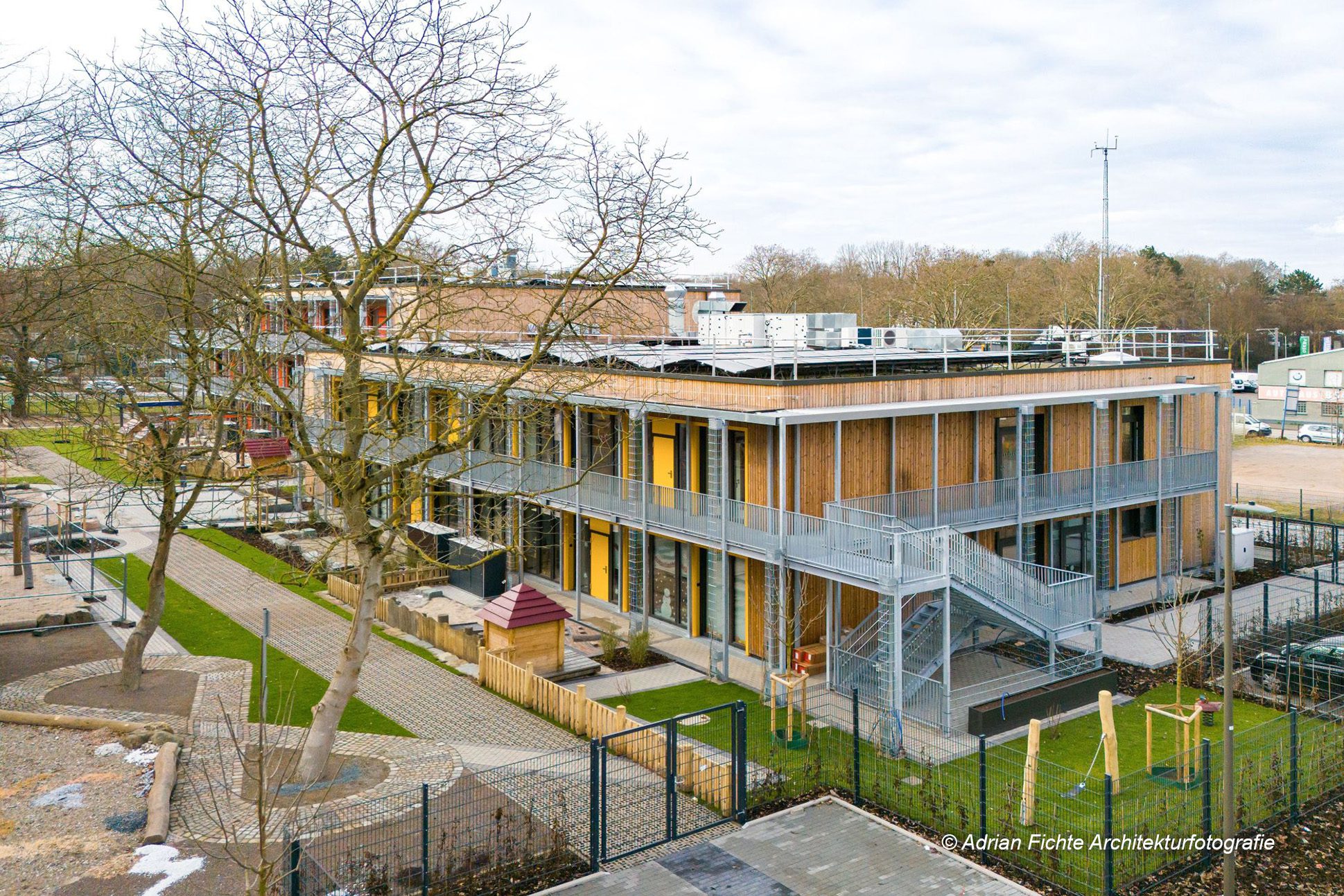 Neues modernes Schulgebäude mit Holz- und Glaselementen, umgeben von einem Spielplatz und Bäumen im Winter.