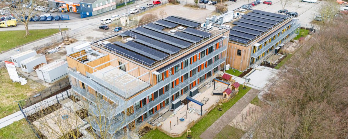 Luftaufnahme eines modernen Gebäudekomplexes mit Solaranlagen und begrüntem Außenbereich.