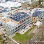 Luftaufnahme eines modernen Gebäudekomplexes mit Solaranlagen und begrüntem Außenbereich.