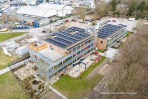 Luftaufnahme eines modernen Gebäudekomplexes mit Solaranlagen und begrüntem Außenbereich.