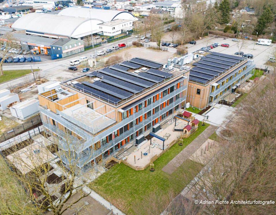 Luftaufnahme eines modernen Gebäudekomplexes mit Solaranlagen und begrüntem Außenbereich.