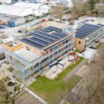 Luftaufnahme eines modernen Gebäudekomplexes mit Solaranlagen und begrüntem Außenbereich.