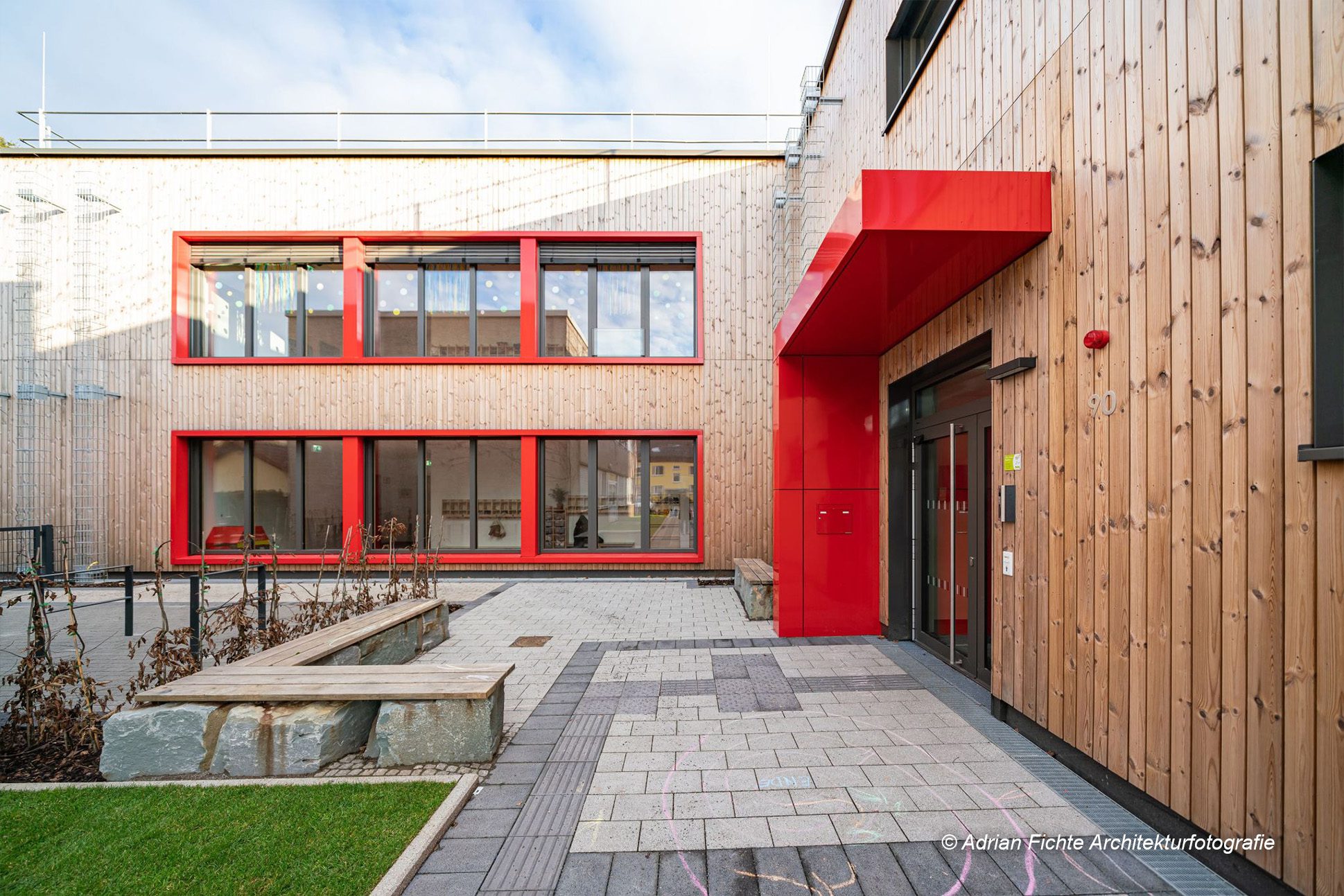 Moderner Holzbau mit roten Akzenten und großzügigen Fensterfronten. Ideal für umweltfreundliche Architekturprojekte.
