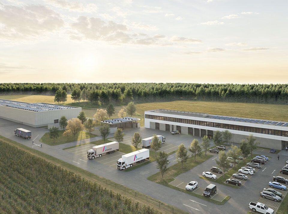 Moderne Logistikzentrale mit Lkw, Solarzellen und Parkplätzen, umgeben von Wald und Feldern unter bewölktem Himmel.